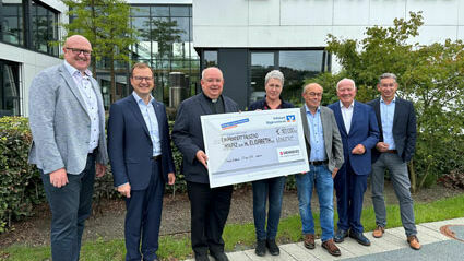 Sechs Männer und eine Frau stehen vor dem Verwaltungsgebäude der Firma MENNEKES Elektrotechnik GmbH & Co. KG. Die Frau und einer der Männer halten einen großen Spendenscheck in der Hand.