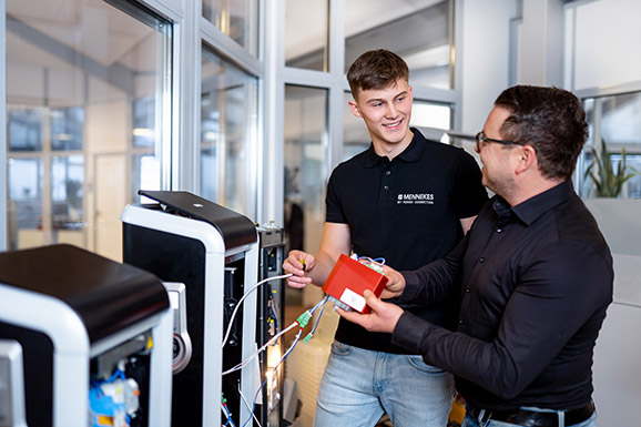 Der männliche Vorgesetzte erklärt einem männlichen Azubi die elektrischen Leitungen in einer Ladesäule