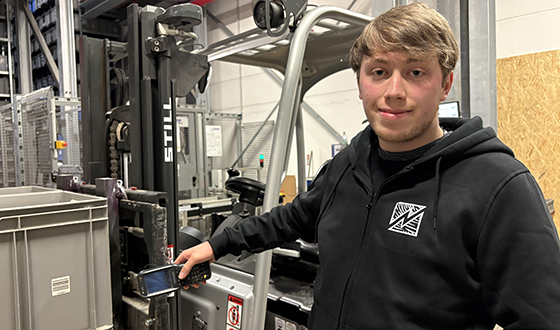 Auszubildender in der Lagerlogistik bedient ein Flurförderzeug und scannt Waren im Lagerbereich.