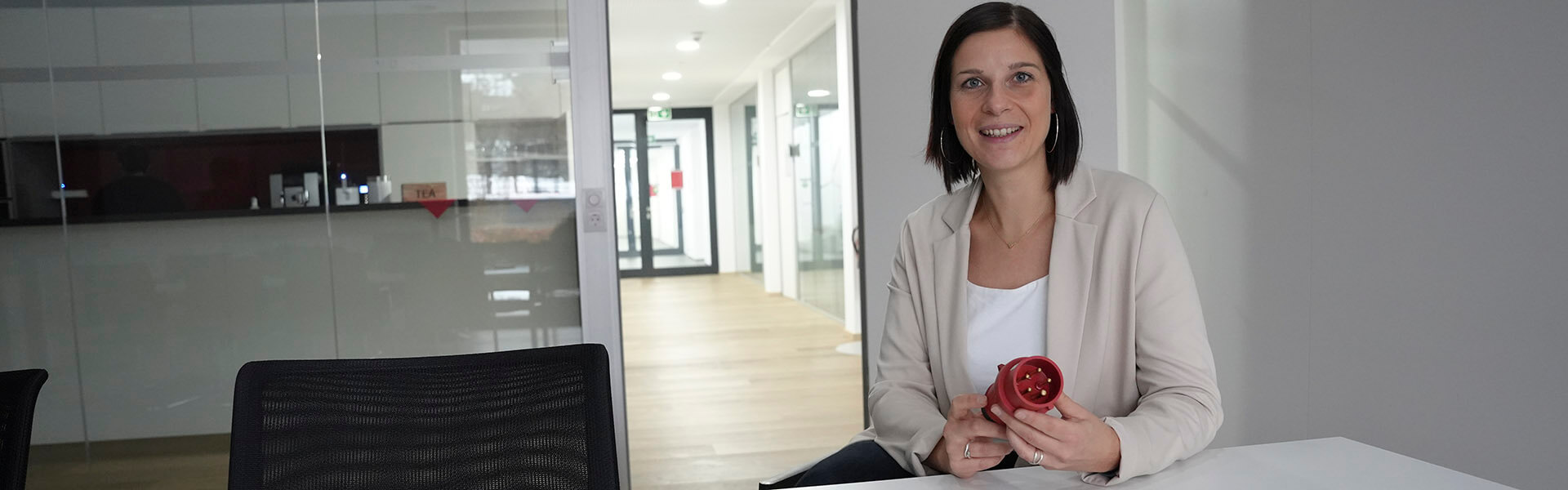 Eine Frau sitzt am Tisch und hält einen roten Industriestecker von MENNEKES in der Hand