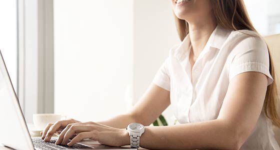 Eine Frau sitzt lächelnd am Tisch und bedient ein Laptop