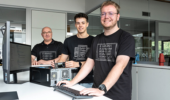 Drei Auszubildende zum Fachinformatiker arbeiten gemeinsam an einem Computerarbeitsplatz in der IT-Abteilung eines Industrieunternehmens.