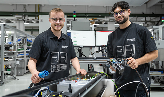 Zwei Auszubildende im Bereich Industrieelektrik montieren und prüfen elektrische Komponenten in der Produktionshalle.