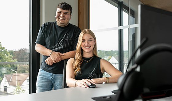 Zwei Auszubildende im kaufmännischen Bereich arbeiten gemeinsam an einem Schreibtisch im Büro eines Industrieunternehmens.
