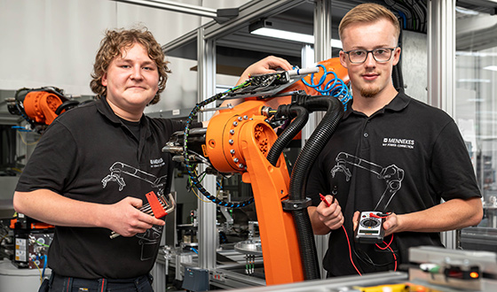 Zwei Auszubildende zum Mechatroniker prüfen einen Industrieroboter mit Messgeräten in der Automatisierungstechnik.
