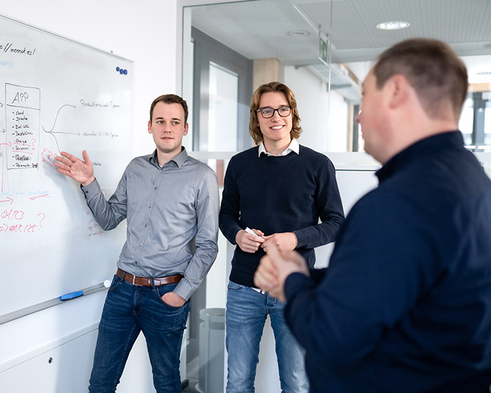 Dei Personen stehen an einem Flipchart und unterhalten sich über eine Zeichnung