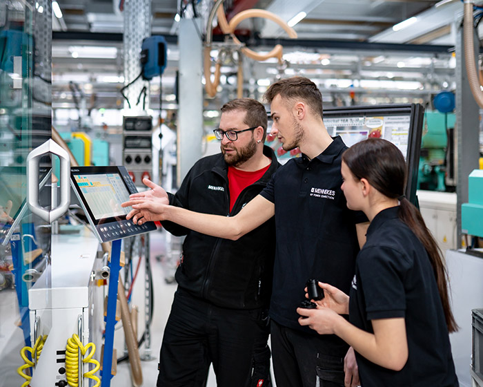 Drei Personen stehen an einer Maschine und schauen auf das Steuerungsdisplay.