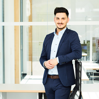 Ein Mann im Anzug lehnt sich an ein Stuhl und lächelt in die Kamera