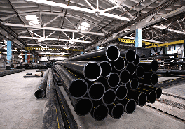 Mehrere schwarze Stahlrohre liegen übereinander in einer Industriehalle