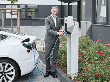 Ein Mann im Anzug steht auf einem Parkplatz und steckt gerade den MENNEKES Stecker zum Laden des Autos an die AMTRON Professional Wallbox auf einer Betonsäule an