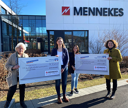 Vier Frau stehen vor dem Verwaltungsgebäude von MENNEKES und halten zwei Spendenschecks in der Hand