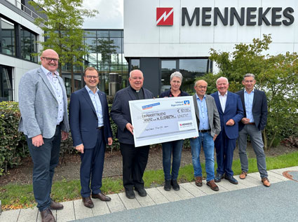 Sechs Männer und eine Frau stehen vor dem Verwaltungsgebäude der Firma MENNEKES Elektrotechnik GmbH & Co. KG. Die Frau und einer der Männer halten einen großen Spendenscheck in der Hand.