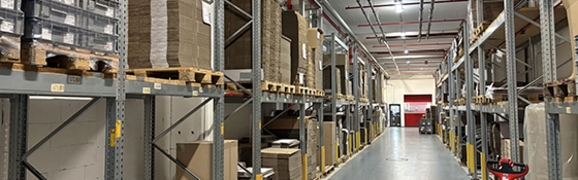 Hochregallager mit Paletten und Waren sowie Flurförderzeug in einem modernen Logistikzentrum.