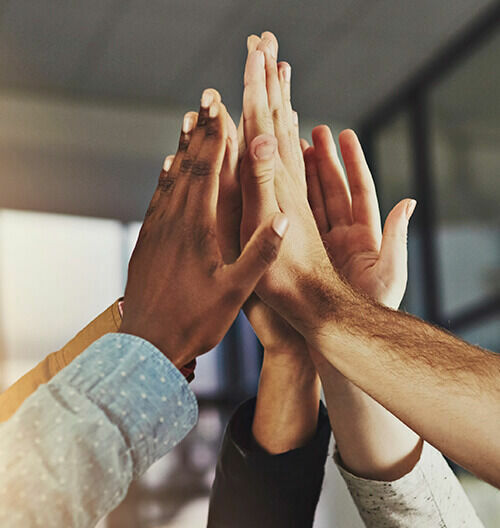 Mehrere Hände unterschiedlicher Personen klatschen im Büro zu einem gemeinsamen High-Five.