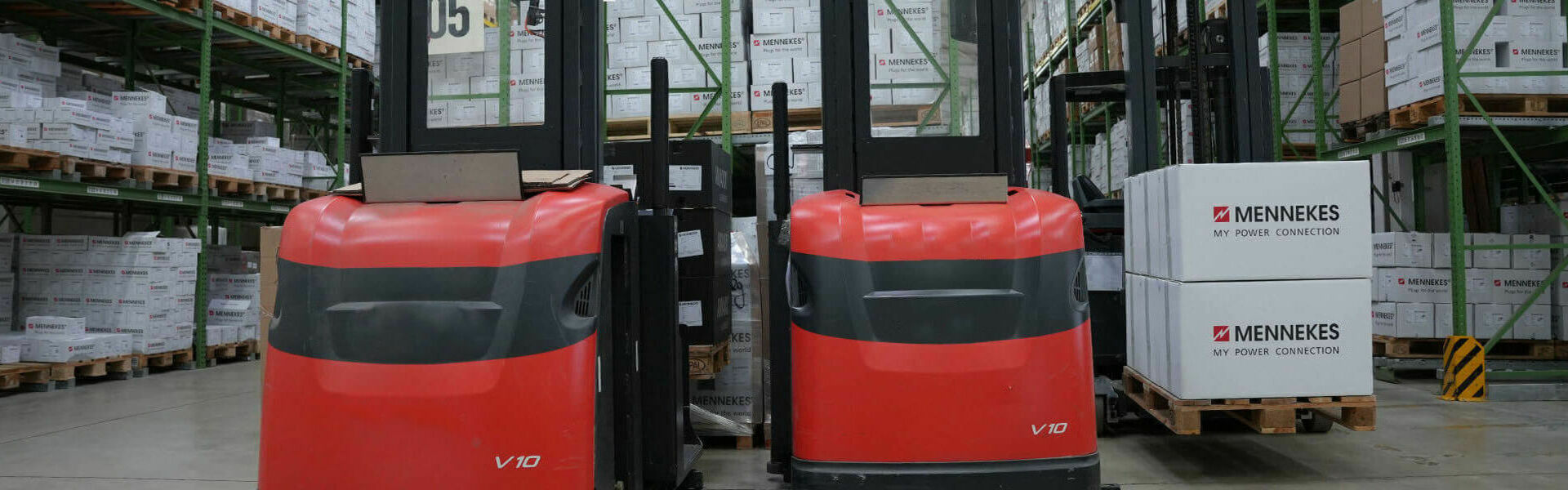 Zwei rote, elektische Hubwagen stehen in einem Lager vor verpackten MENNEKES Kartons