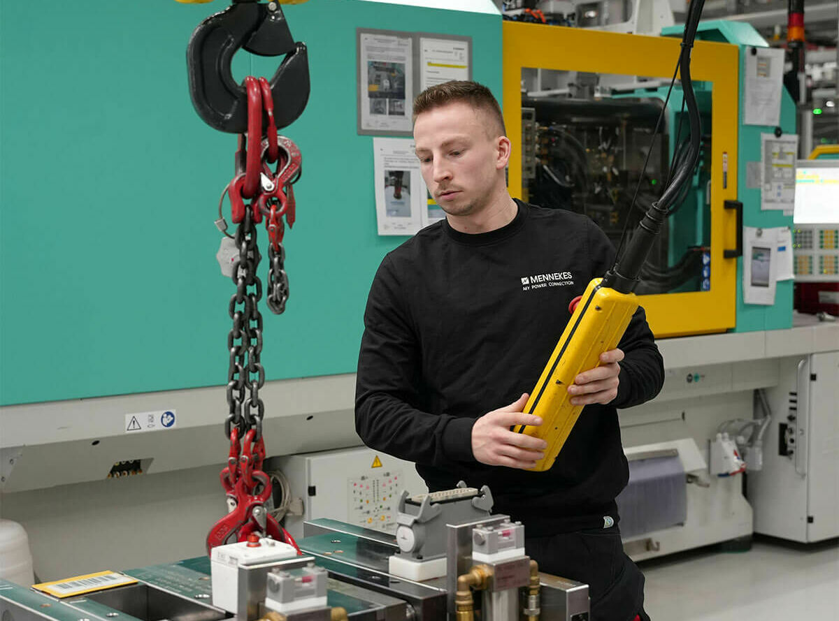 Eine männliche Person im schwarzen Pullover hebt mit Hilfe eines Krans ein Werkzeug im Werkzeugbau