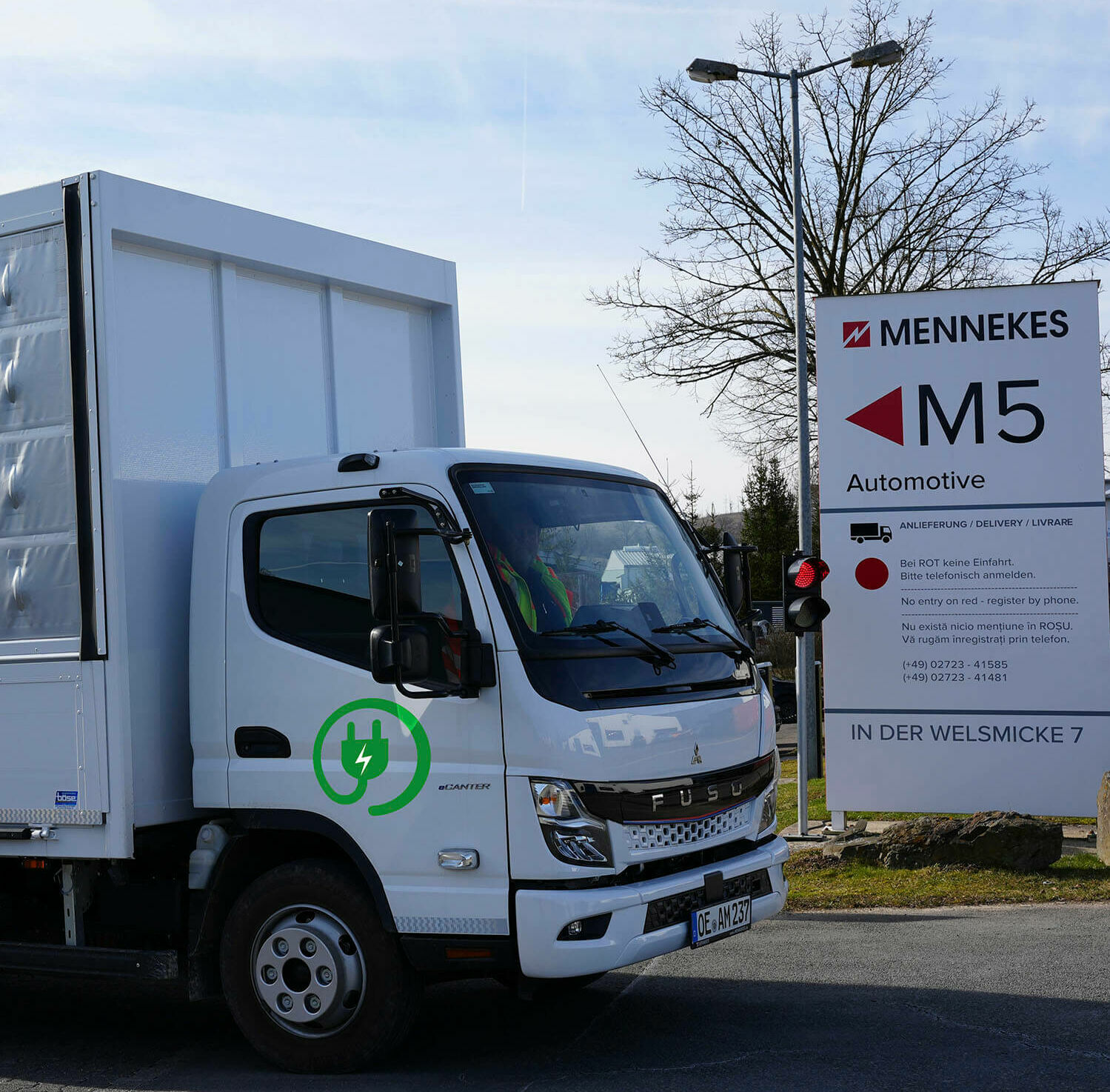 Weißer Elektro-Lkw mit grünem Steckersymbol passiert MENNEKES-Schild „M5 Automotive“.